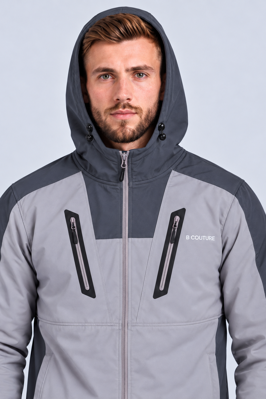 A man wearing a gray and dark gray hooded jacket with black zipper details and the brand name 'B COUTURE' on the chest, set against a light gray background.