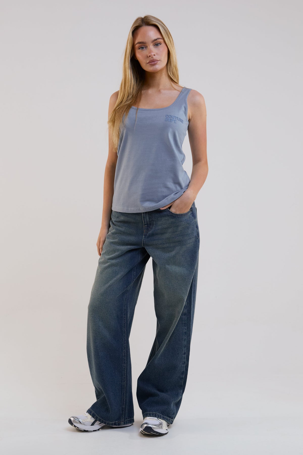 Woman wearing a blue tank top and jeans on a white background