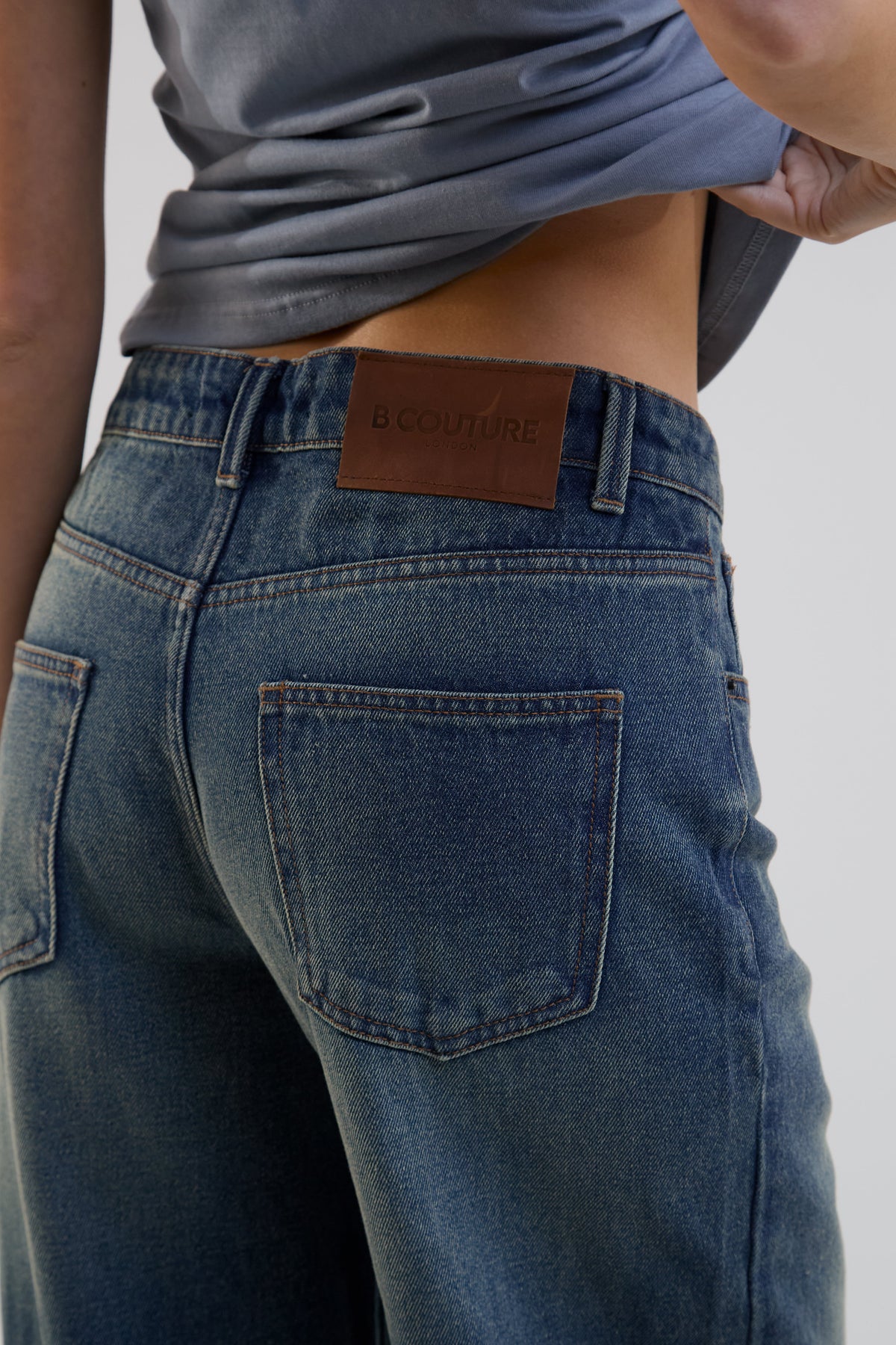Person wearing blue jeans with a brand label on a plain background