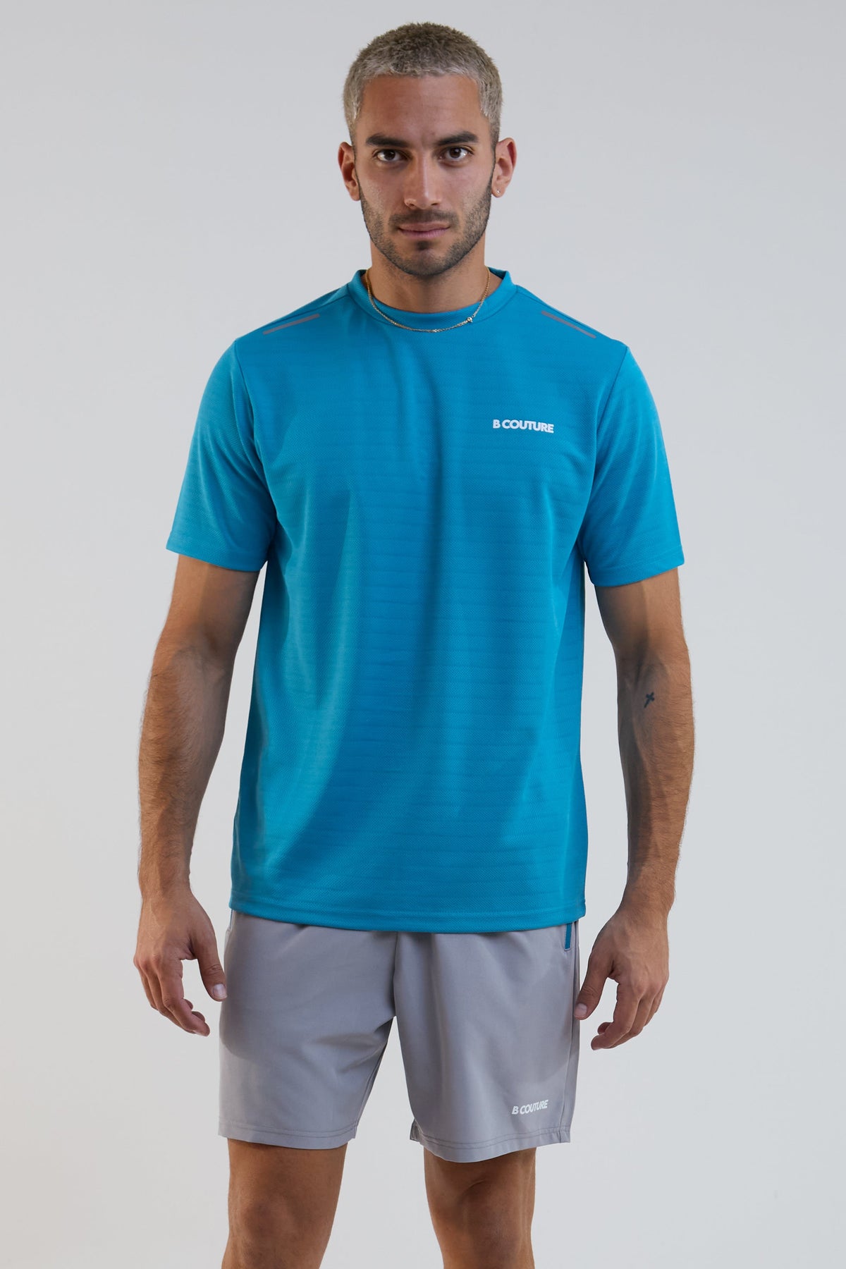 Man wearing a blue athletic shirt and gray shorts on a white background