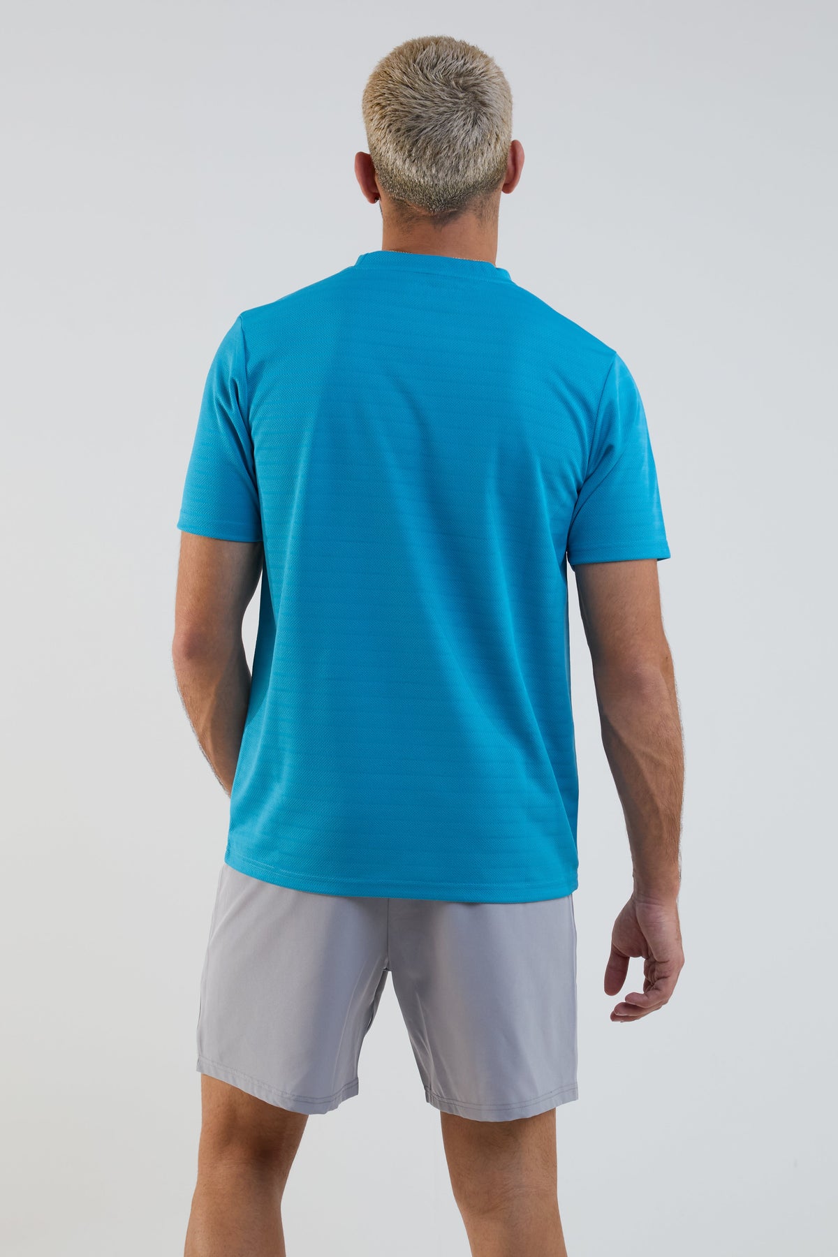 Man wearing a blue t-shirt and gray shorts on a light gray background
