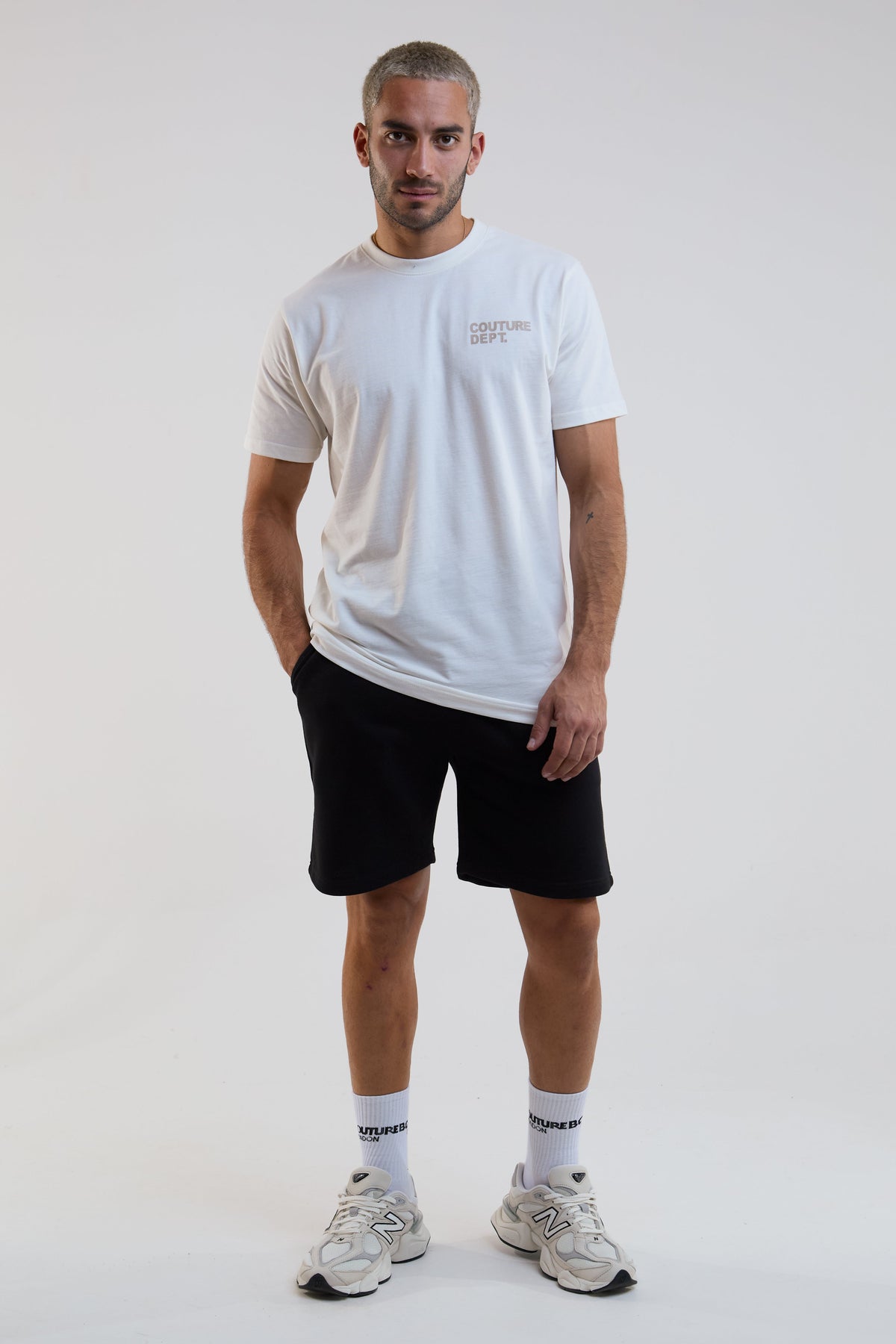 Man wearing a white t-shirt, black shorts, and white sneakers on a plain background