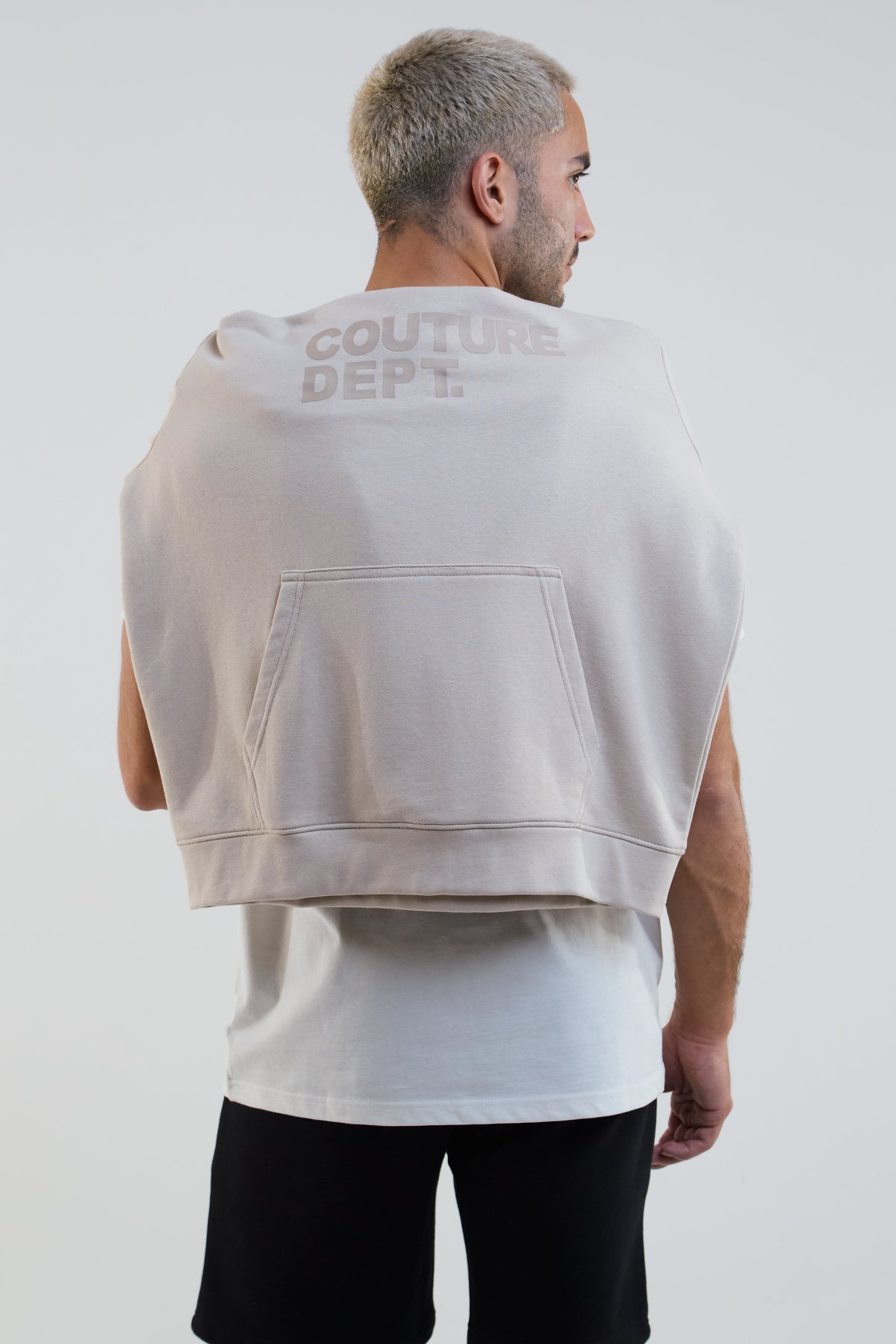 Man wearing a beige sleeveless hoodie with 'Couture Dept.' text on the back against a white background
