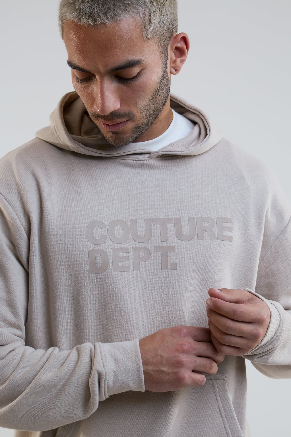 Man wearing a beige hoodie with 'Couture Dept.' text on a plain background