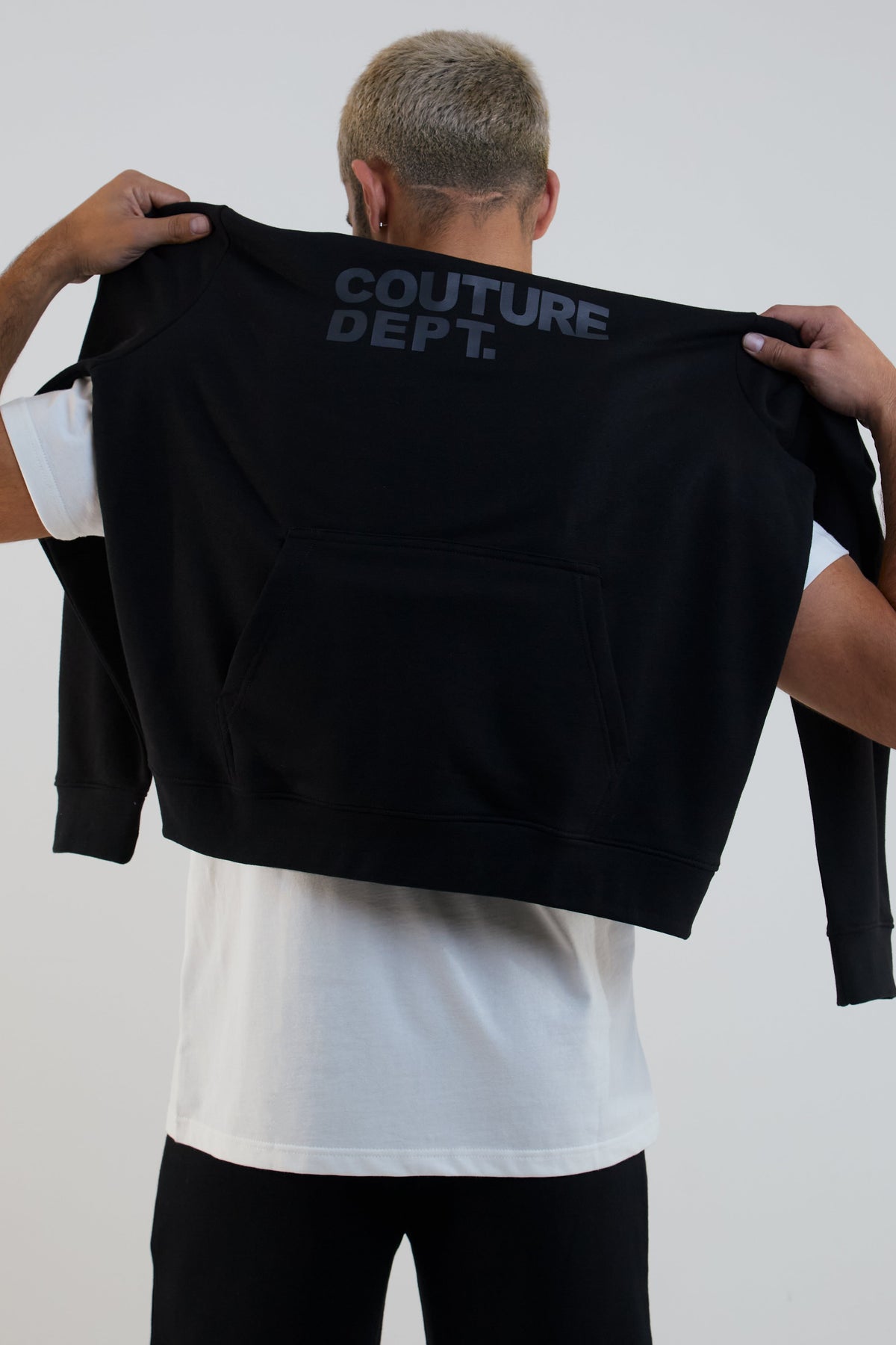 Person holding a black crop top with 'COUTURE DEPT.' text on a plain background
