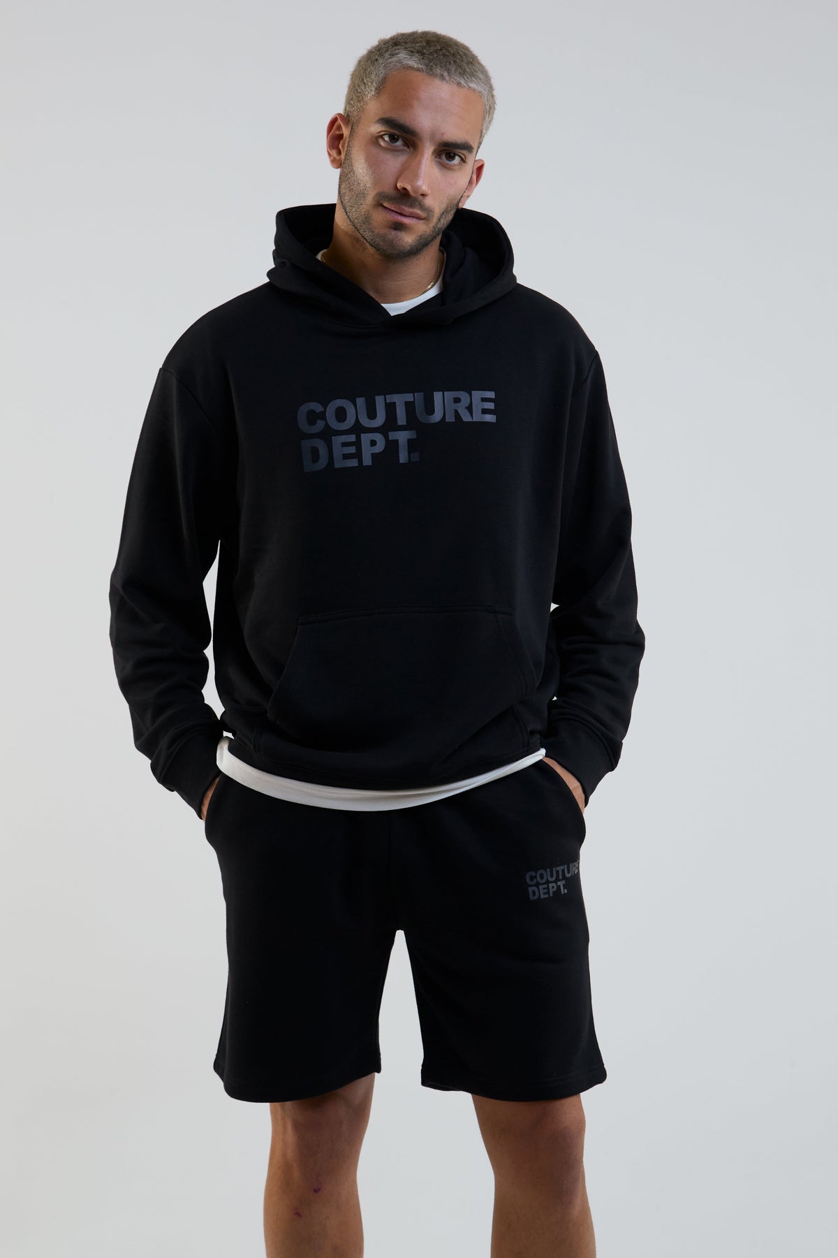 Man wearing a black hoodie with 'COUTURE DEPT' text and matching shorts on a light gray background