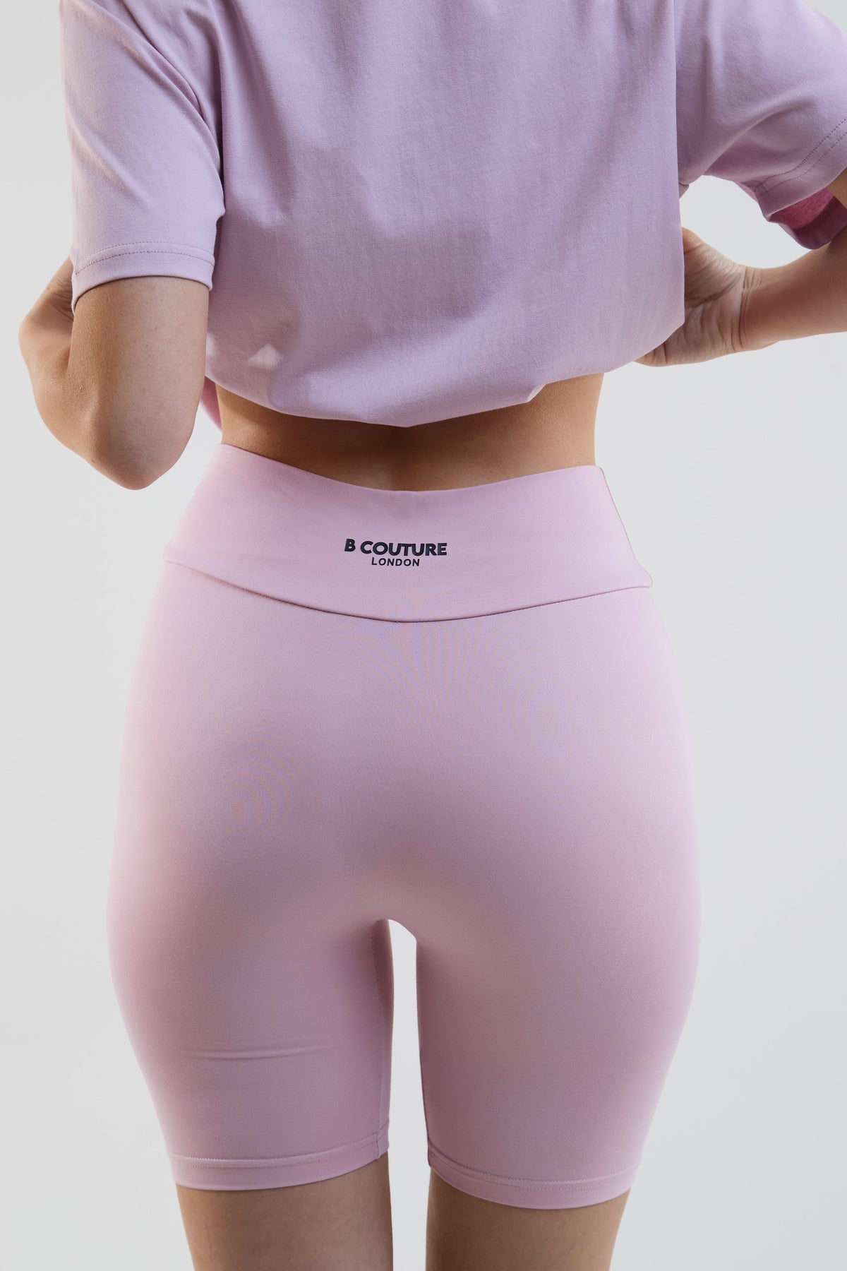 Person wearing pink high-waisted leggings with a visible brand logo on a light gray background