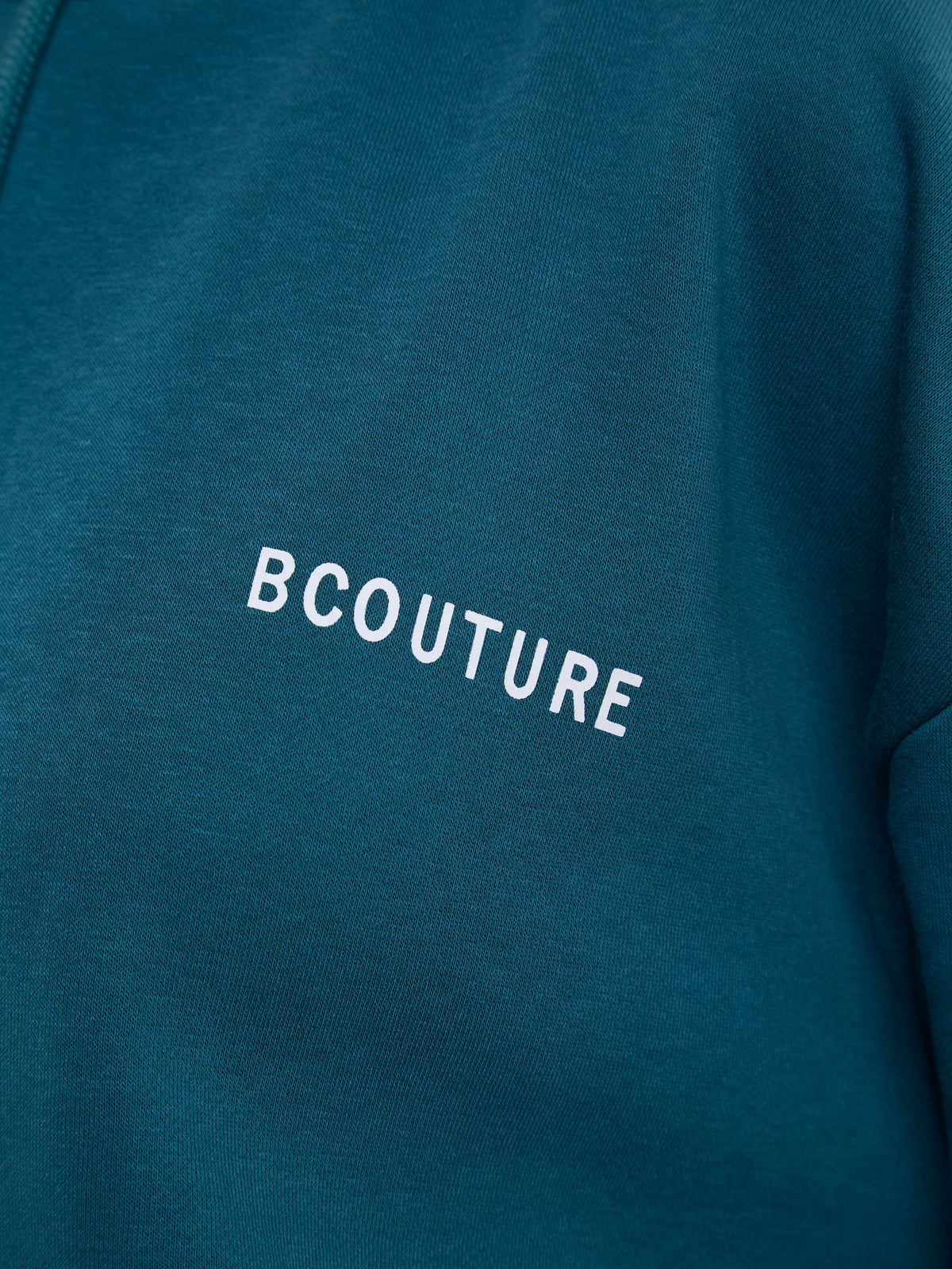 Close-up of a teal blue sweatshirt featuring the word 'BCOUTURE' printed in white across the chest.