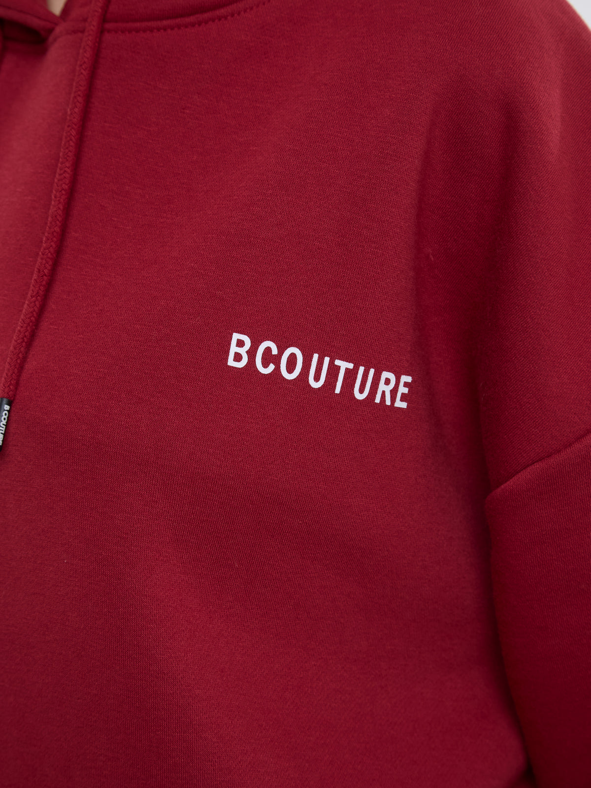A close-up of a red hoodie featuring the brand name 'BCOUTURE' embroidered in white capital letters on the chest.