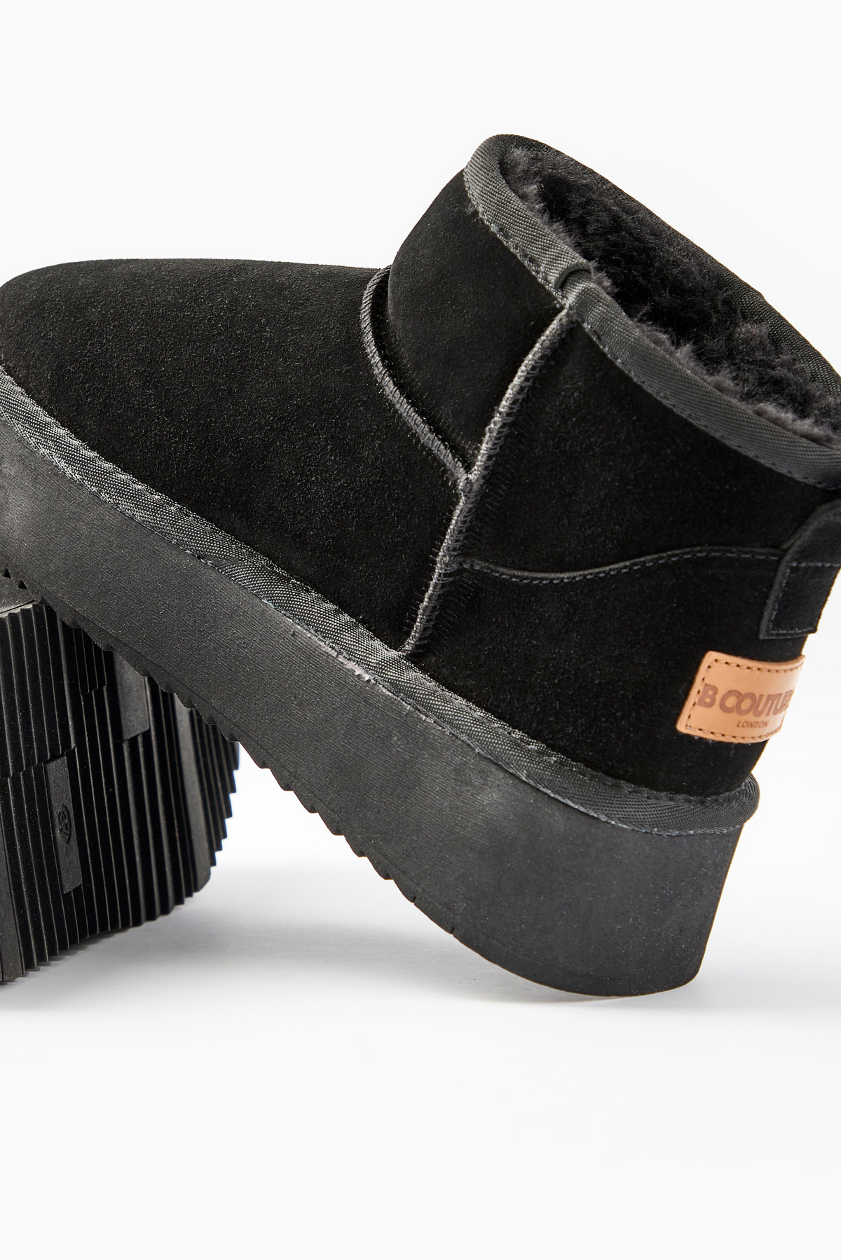 A close-up of the Amwell Genuine Suede Mini Boots in black, featuring a platform rubber sole and a brown leather brand patch on the heel, shown against a white background.