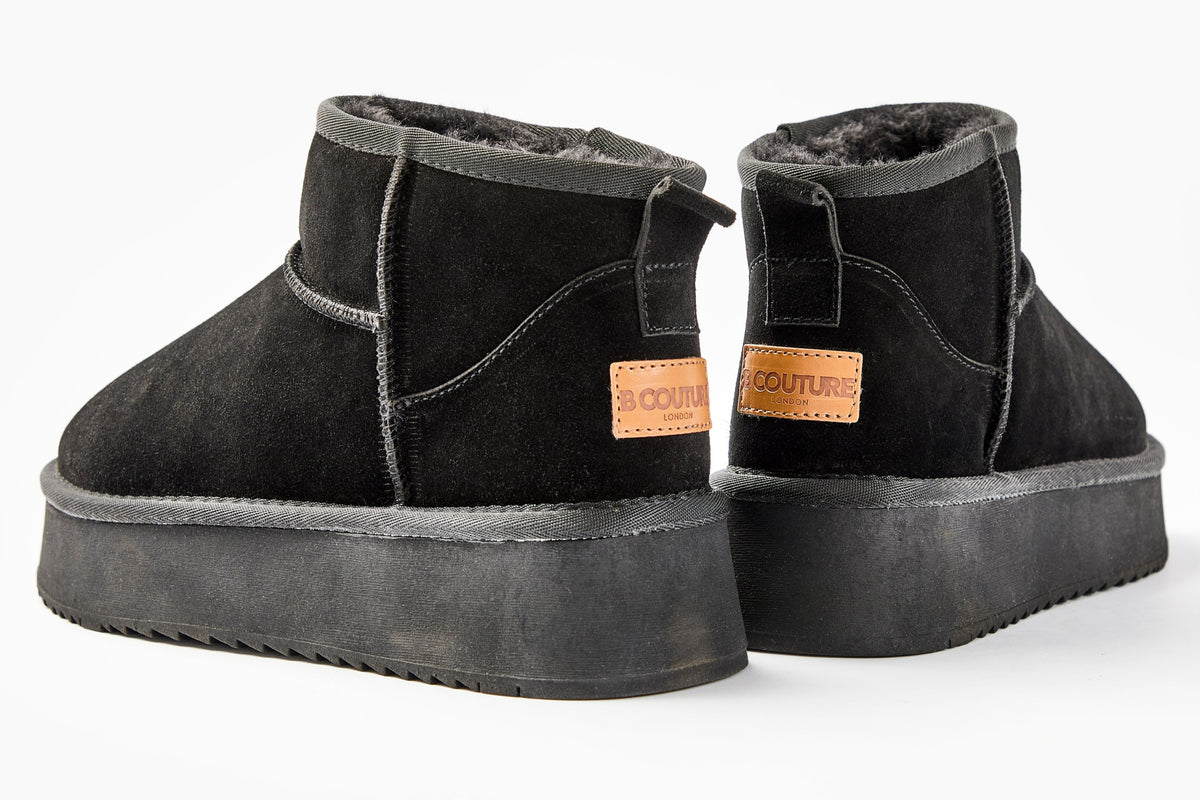 The Amwell Genuine Suede Mini Boots in black feature platform rubber soles and brown leather Couture labels on the back, delivering winter comfort and style. Shown here against a white background.