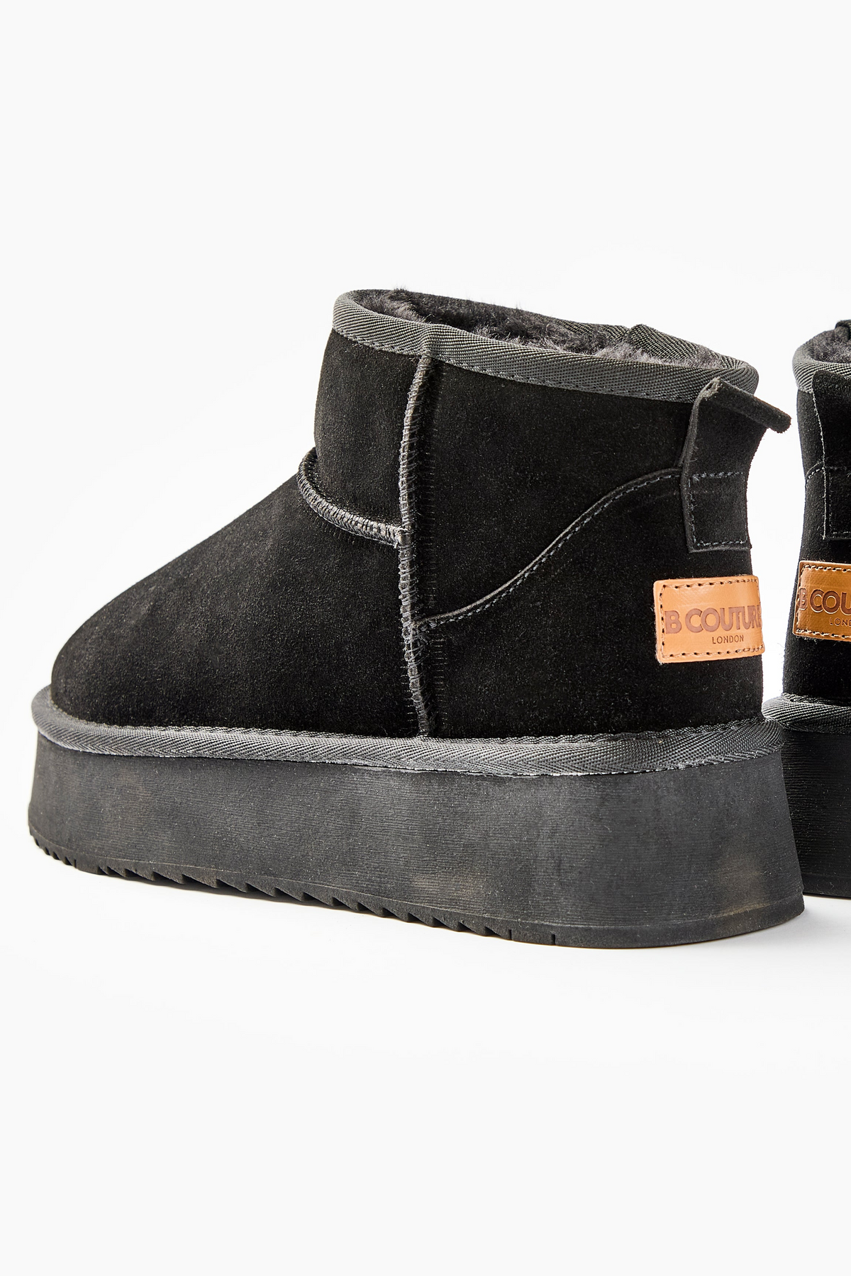 Amwell Genuine Suede Mini Boots - Black: A pair of black suede ankle boots with platform rubber soles, visible stitching, and a brown leather patch with text on the heel—perfect for stylish winter comfort.