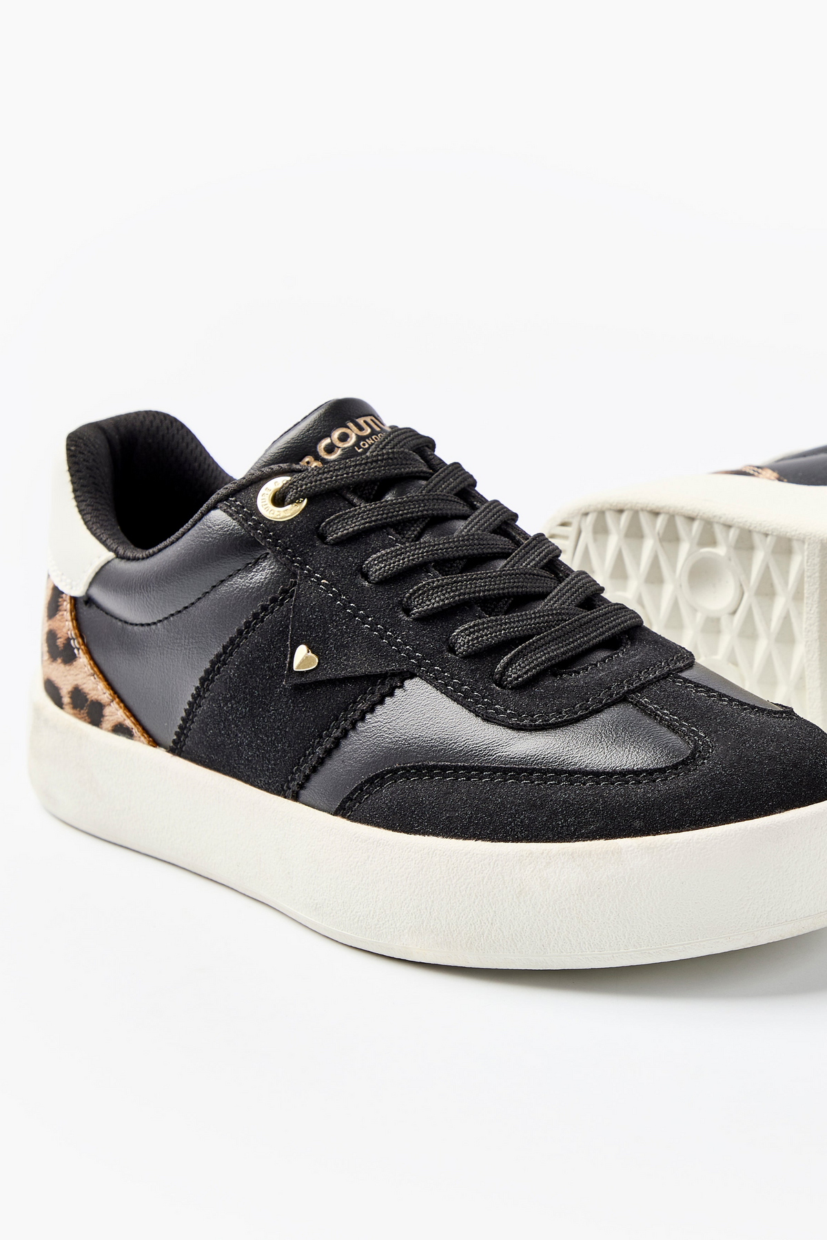 The Ampton Low-Profile Trainer in Black/Leopard features black uppers, white soles, black laces, gold eyelets, a small gold heart detail, a leopard print heel accent with a white patch—blending vintage and modern styles.