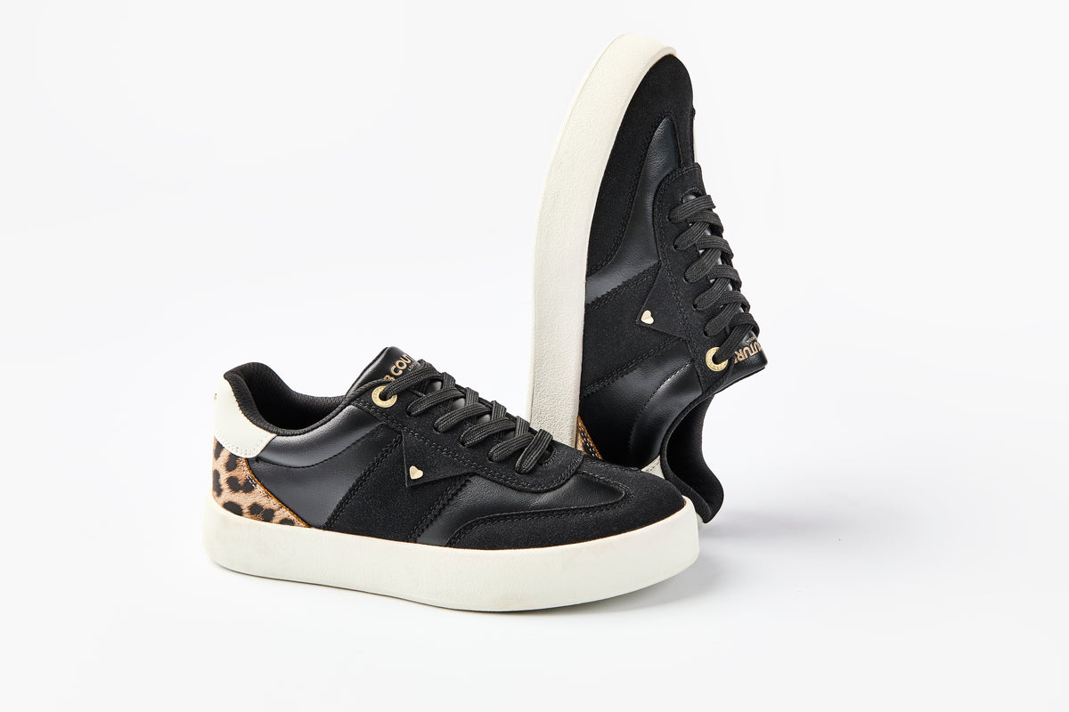 The Ampton Low-Profile Trainer in Black/Leopard features white soles, gold accents, and leopard print near the heel. Displayed on a white background, one shoe stands upright while the other lies on its side, highlighting its vintage appeal.