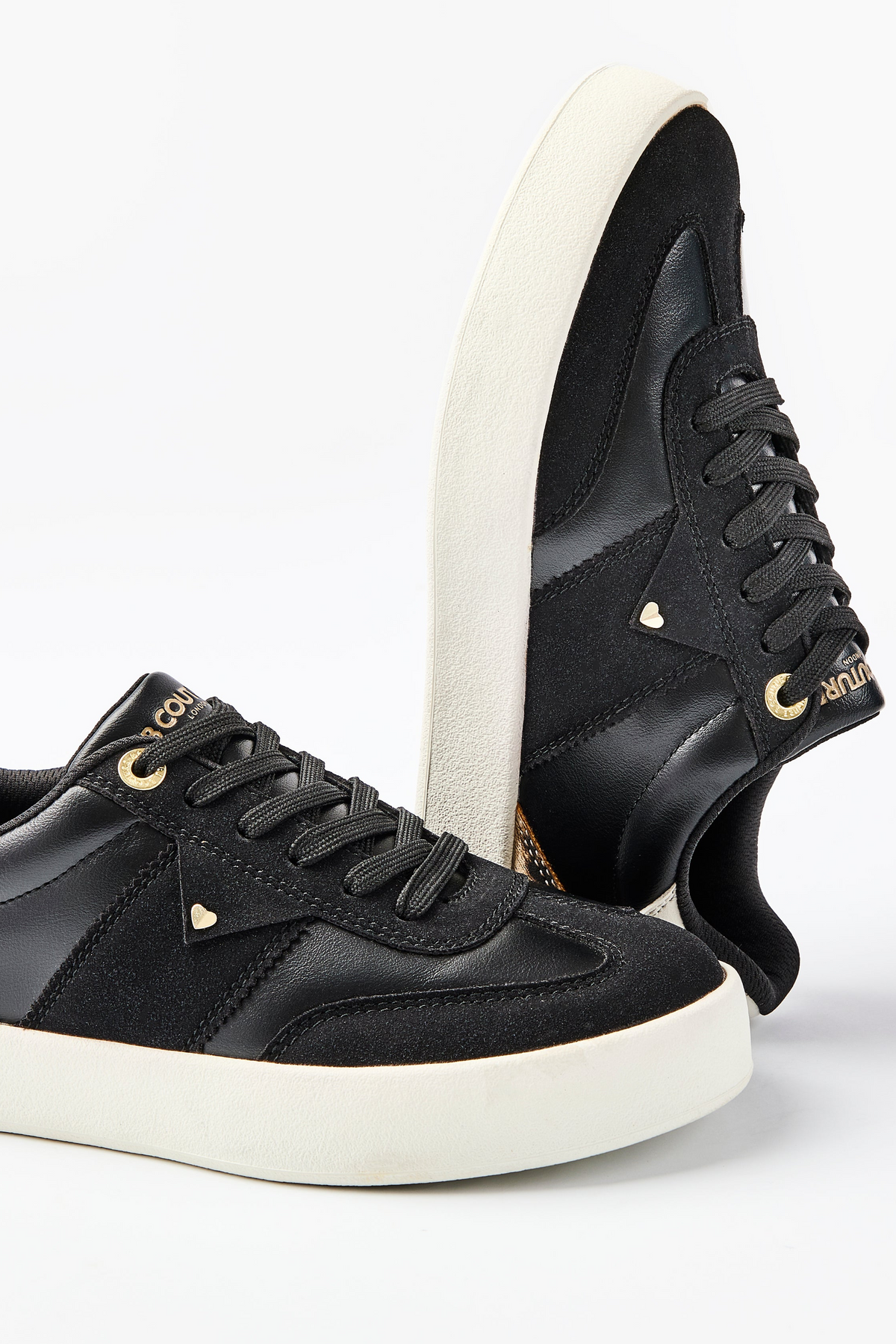 The Ampton Low-Profile Trainer in Black/Leopard features black uppers, white soles, gold branding, black laces, and a subtle vintage look. Displayed on a white background with one shoe upright and the other lying flat.