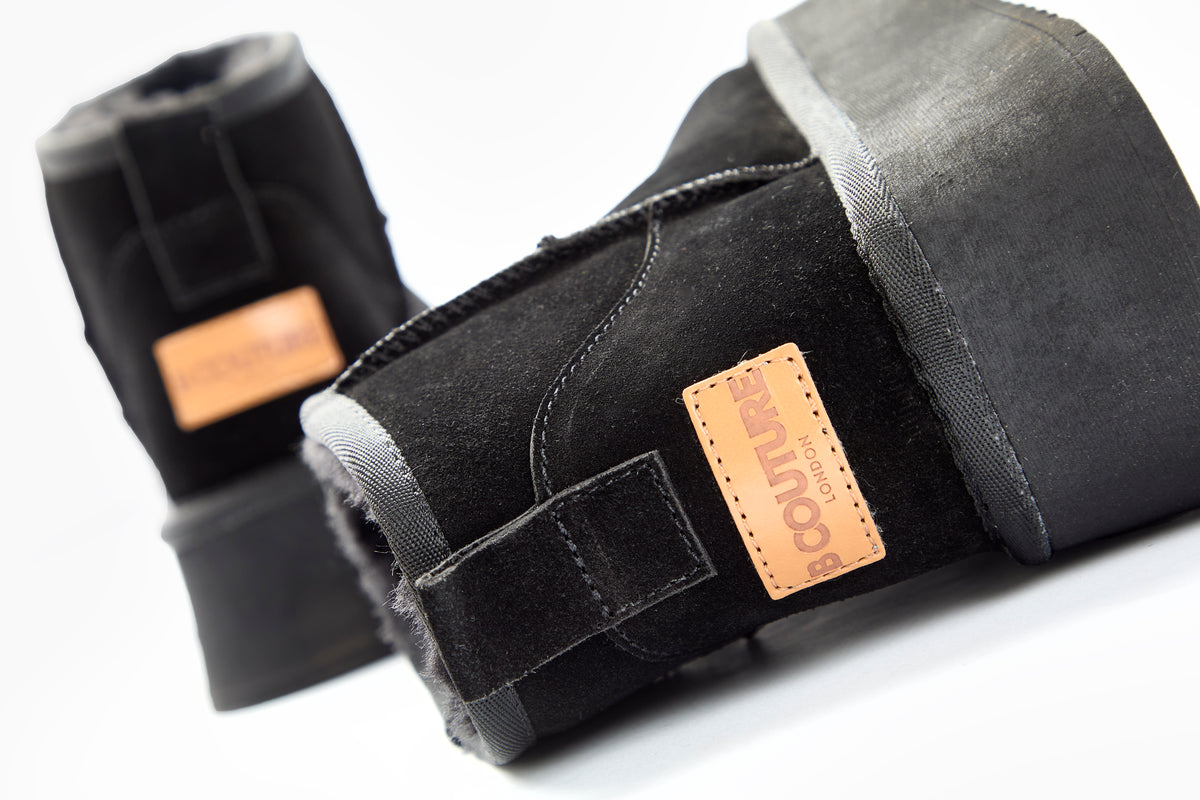 Close-up of two Amwell Genuine Suede Mini Boots in black with thick platform rubber soles and tan leather patches labeled COUTURE LONDON on the back, set against a white background for ultimate winter comfort.